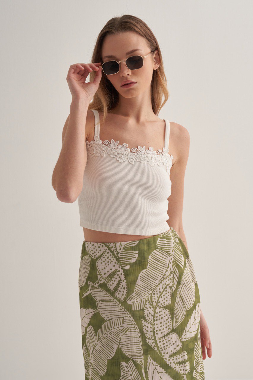 Woman wearing a green tropical leaf print midi skirt paired with a white crop top and sunglasses.