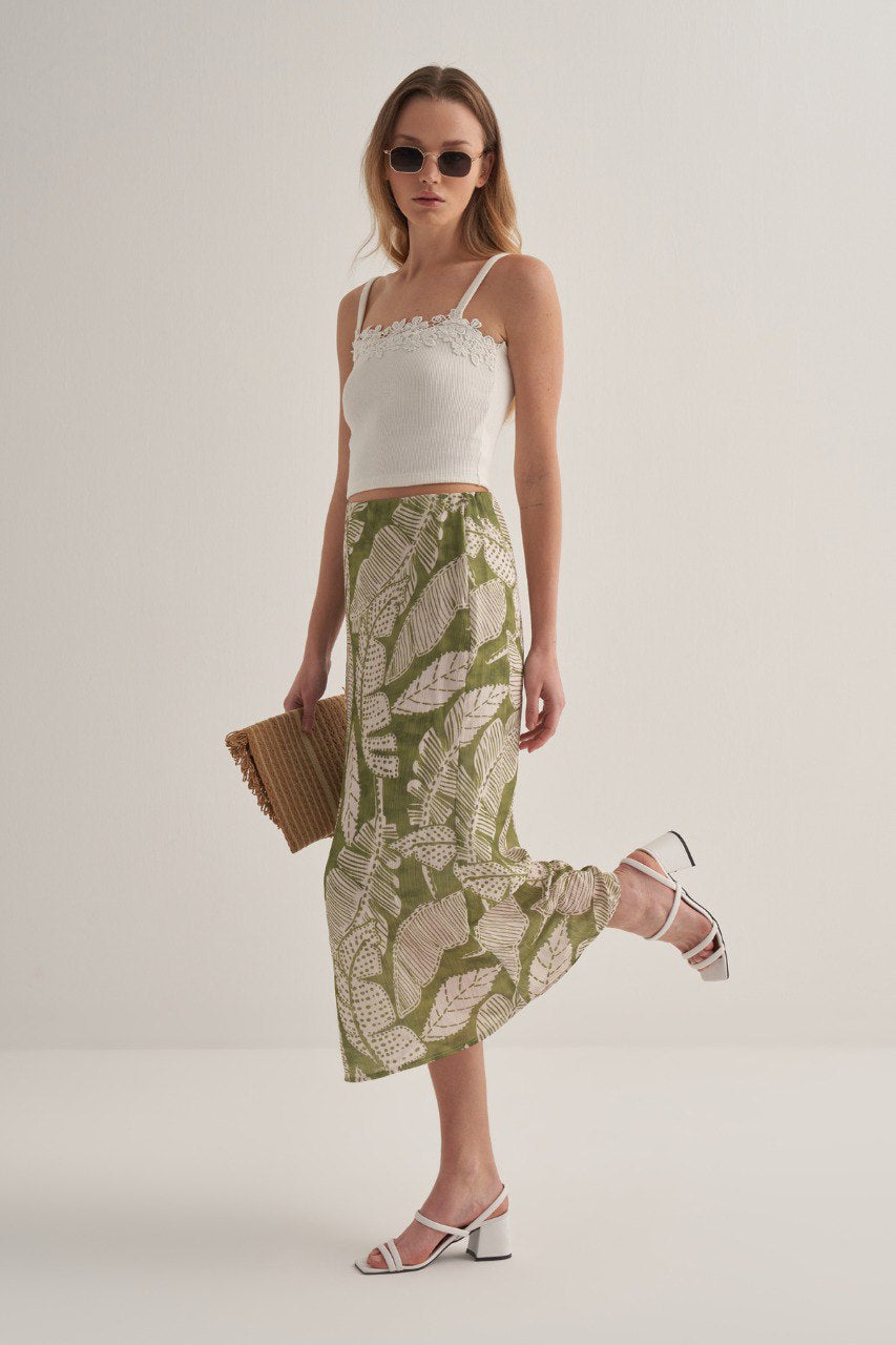 Full outfit view of green botanical print skirt styled with white block heel sandals and a woven clutch.